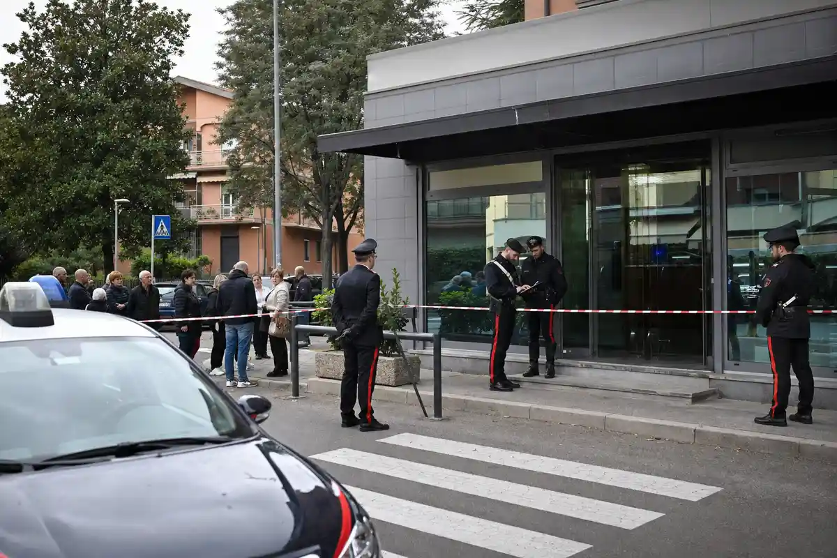 Carabinieri davanti all’ingresso di una banca con nastro di interdizione e passanti a distanza