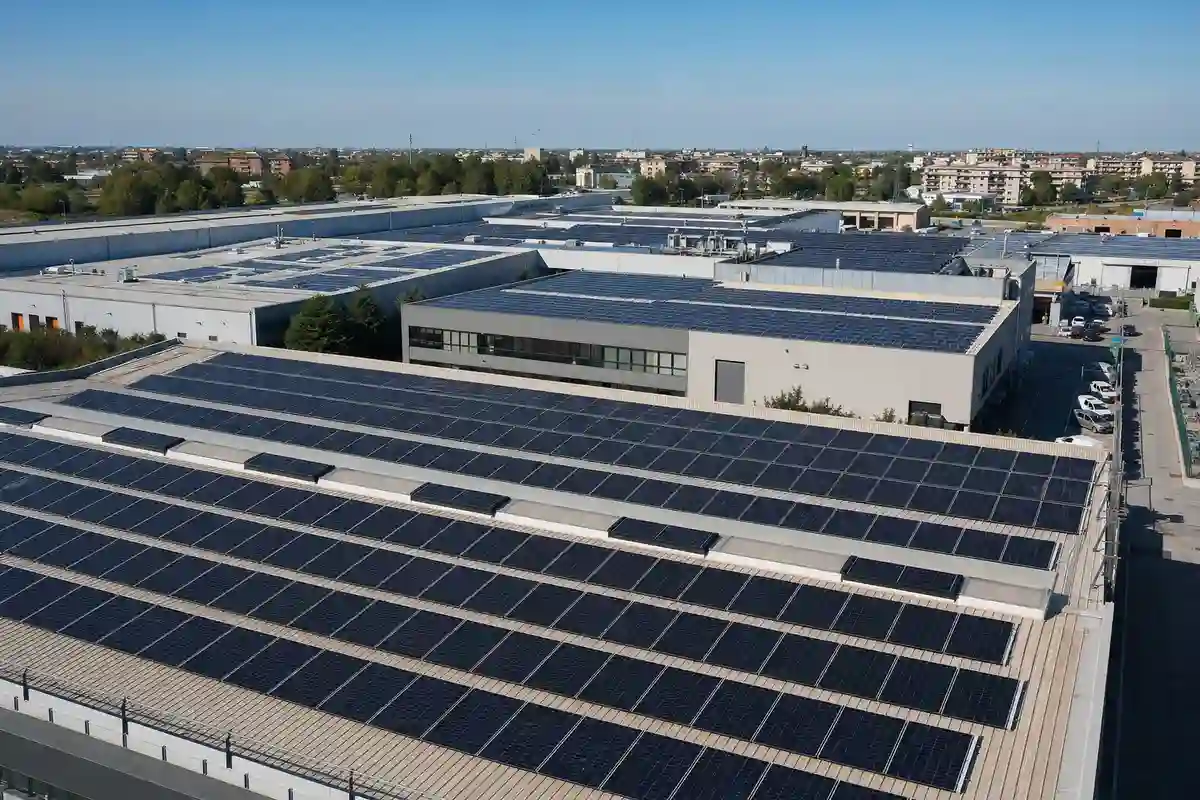 Tetti di capannoni industriali con pannelli fotovoltaici in file ordinate, con area urbana sullo sfondo