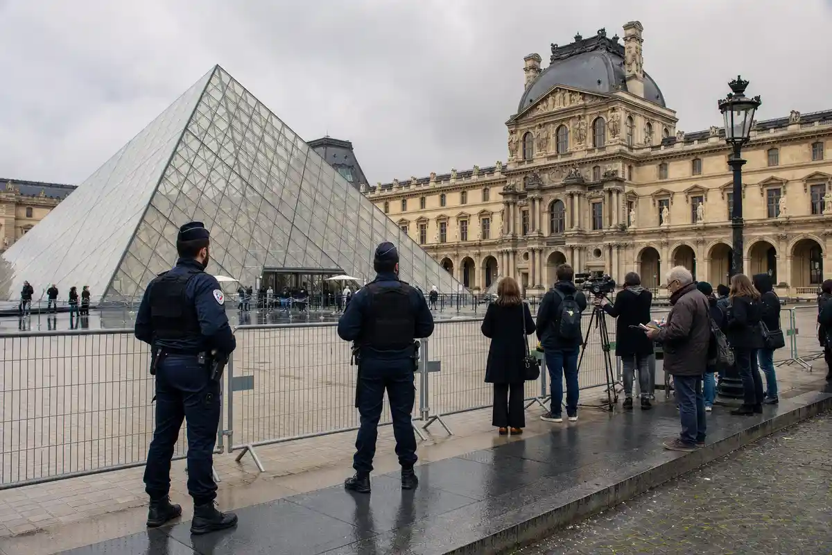 Piramide del Louvre con agenti di polizia e giornalisti dietro transenne in una giornata grigia a Parigi