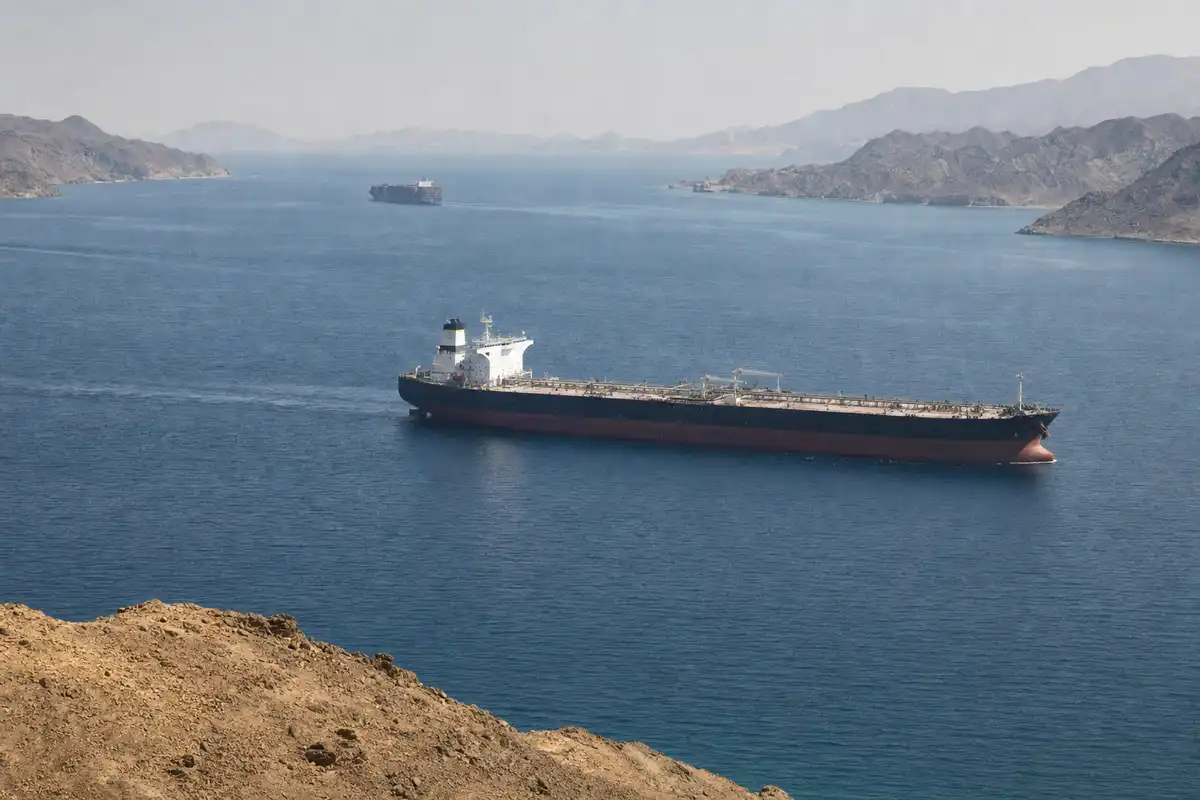 Petroliera in primo piano e nave portacontainer in lontananza in un canale marittimo tra coste aride