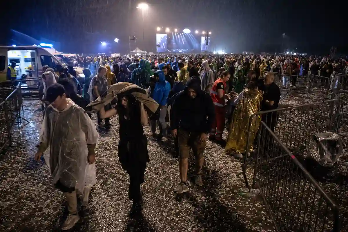 Folla in impermeabili evacua un concerto notturno sotto grandine e pioggia, con ambulanza e transenne