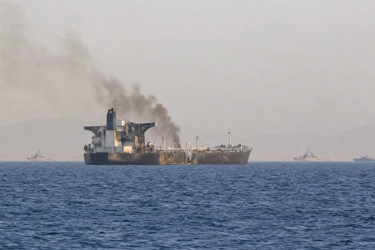 Nave mercantile danneggiata in mare con fumo nero che si alza dallo scafo e unità navali lontane