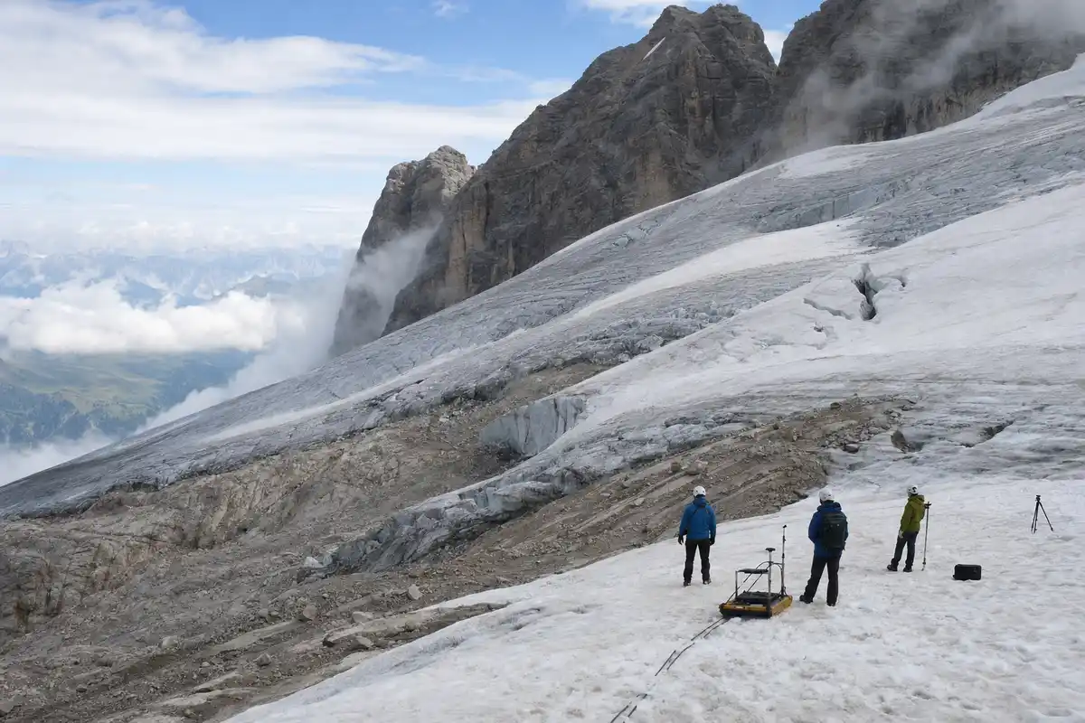Ricercatori su un ghiacciaio fratturato con crepacci, detriti e pareti rocciose in alta quota