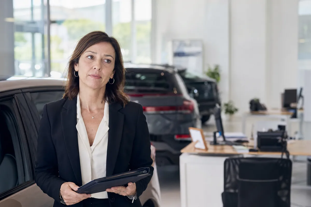Venditrice d’auto con tablet in una concessionaria luminosa, con auto e scrivanie sullo sfondo