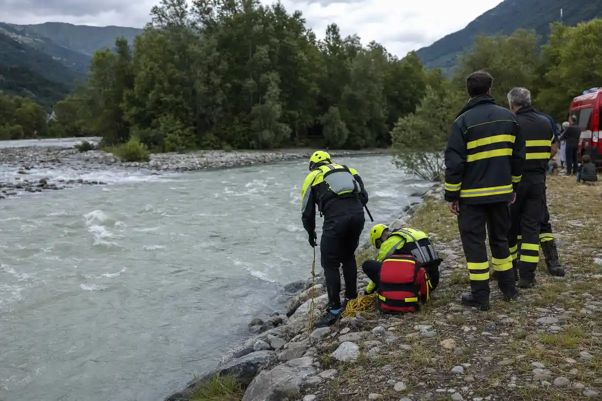 Soccorritori e vigili del fuoco sulla riva di un fiume in piena con corde e zaino di salvataggio