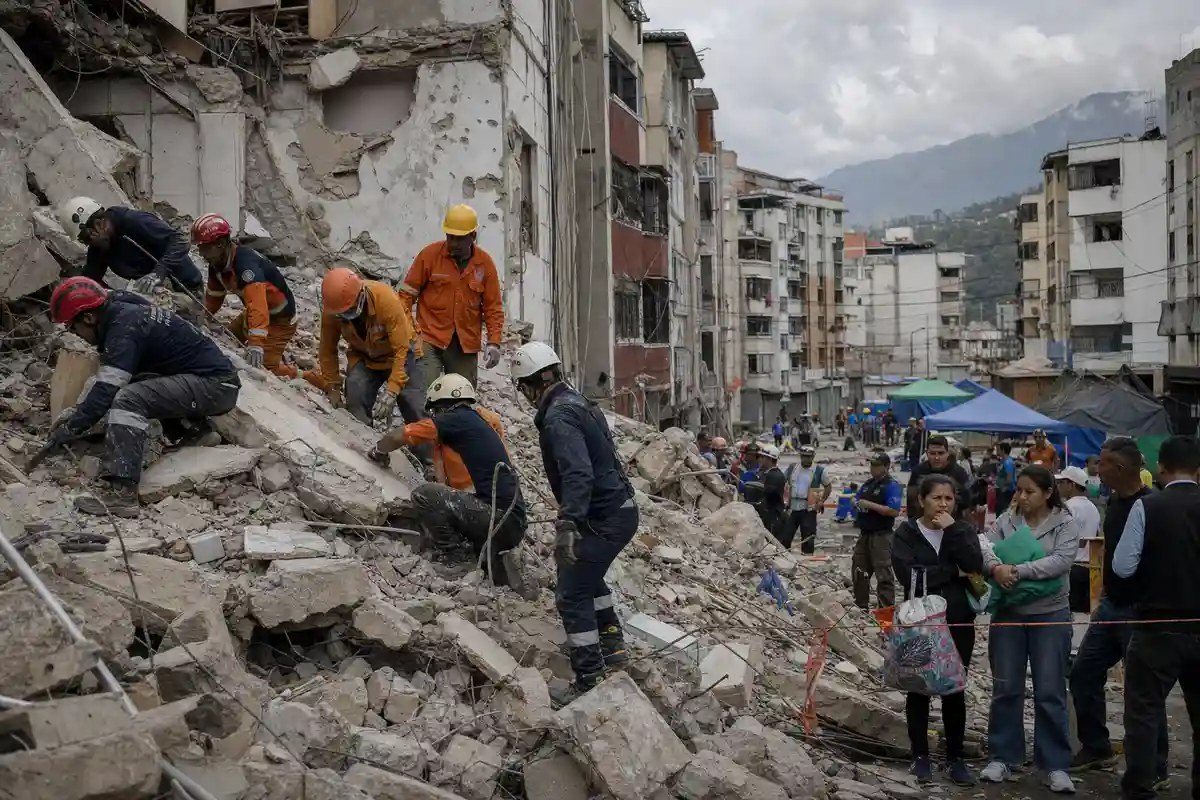 Soccorritori al lavoro tra le macerie di un palazzo crollato, mentre residenti osservano dietro una barriera