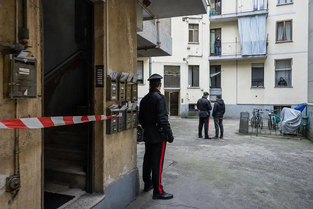Cortile di palazzina con nastro di sequestro all’ingresso, cassette della posta piene e carabinieri in servizio