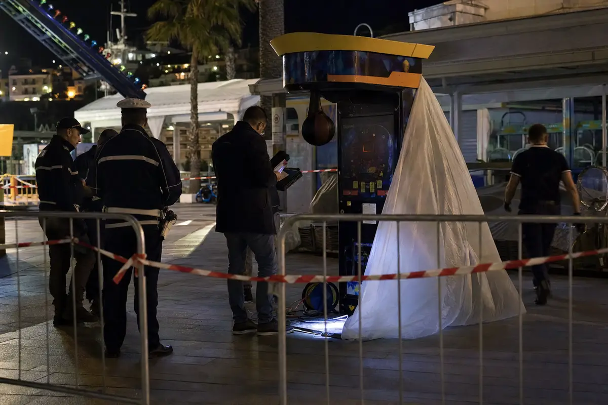 Luna park di notte con transenne e nastro rosso-bianco, agenti al lavoro vicino a una macchina punchingball isolata