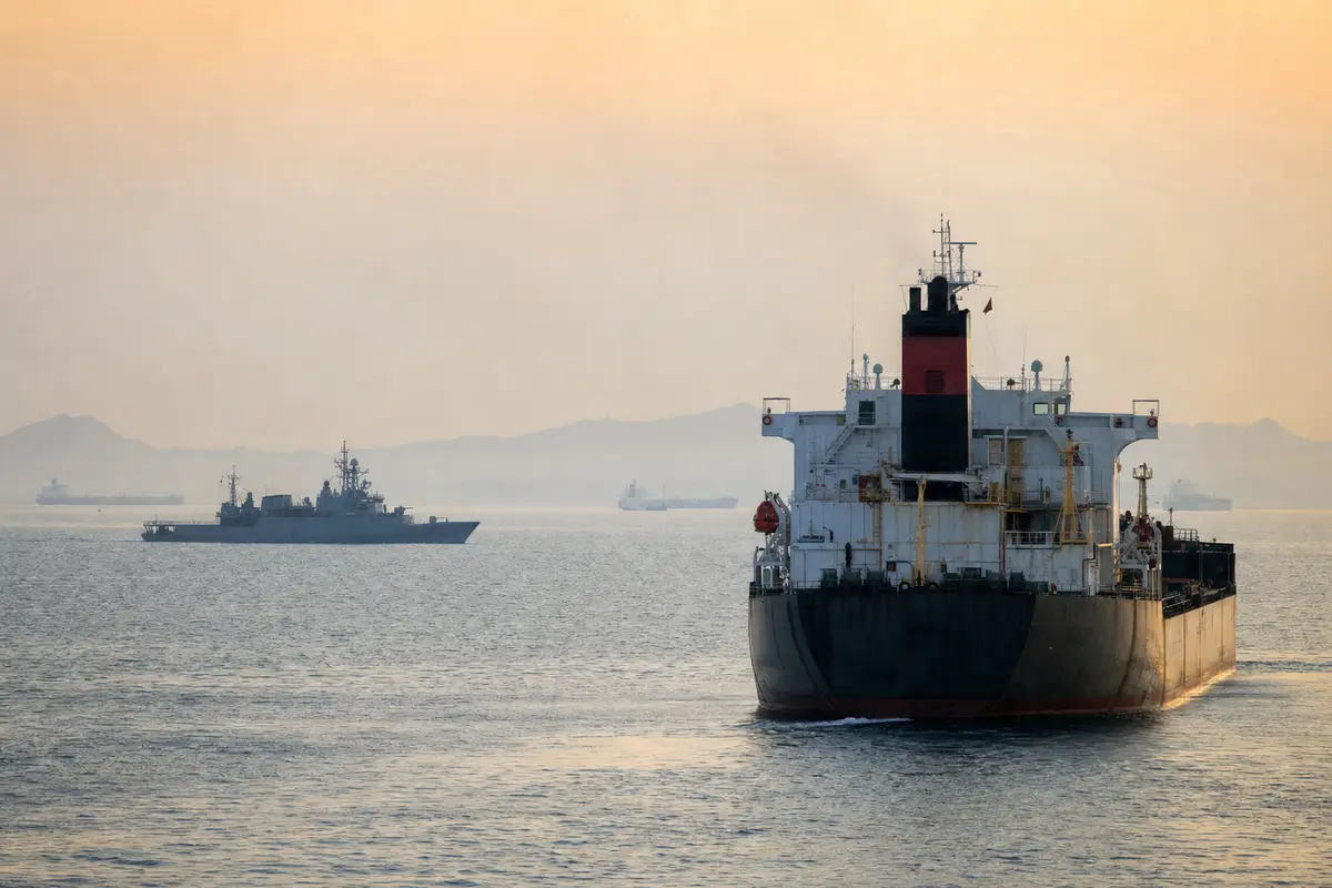 Petroliera in primo piano e nave militare di pattugliamento sullo sfondo in mare all’alba