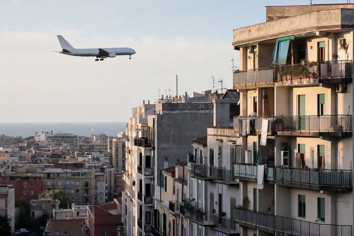 Aereo di linea in volo basso sopra palazzi residenziali con balconi e bucato in una città costiera